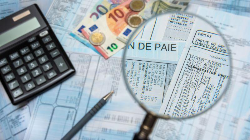 Calculatrice, billets en euros et loupe sur un bulletin de paie